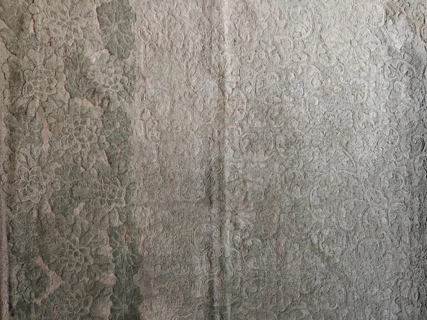 Close-up of a distressed green and gray rug with a high-low floral and scroll pattern texture.