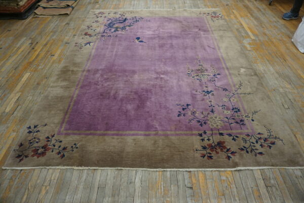 A large purple and taupe rug with floral and stylized bird motifs lies on worn wood floorboards.