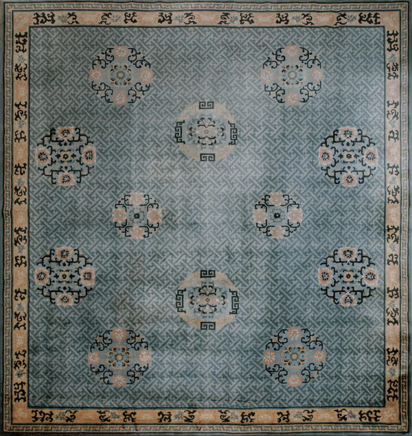Dusty blue rug with a geometric lattice pattern, peach floral medallions, and a tan patterned border.