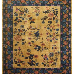 A gold, high-pile rug with blue, rust, and pink sprawling florals inside a dense navy botanical border.