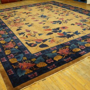 Low-pile rug with a gold field and dark blue border featuring colorful pink and blue floral designs.
