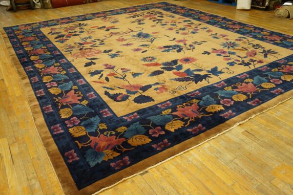 Low-pile rug with a gold field and dark blue border featuring colorful pink and blue floral designs.
