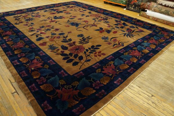 Camel-toned rug features a low pile, a navy border, and a multicolored scrolling floral pattern on wooden floors.
