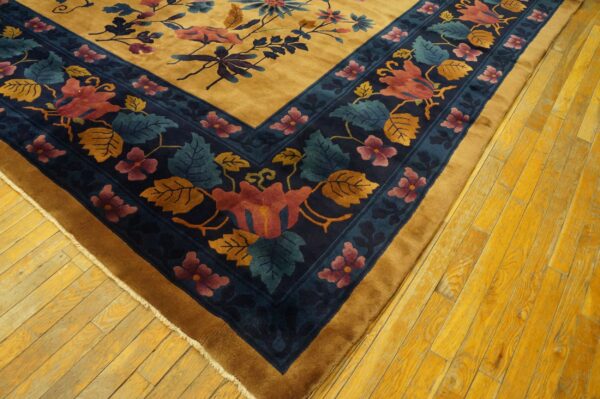 Plush gold rug corner featuring a dark blue border with red, pink, and teal floral designs on wood floors.