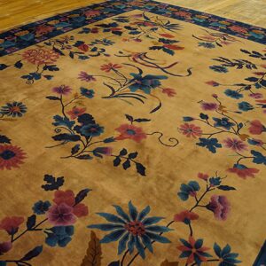 Golden rug with visible sheen and scattered pink and blue floral designs and a dark border on wood floor.