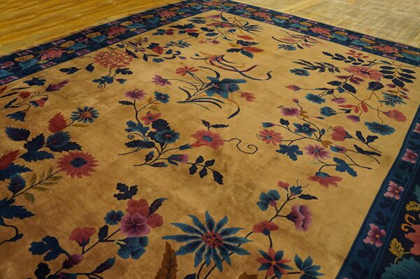 Golden rug with visible sheen and scattered pink and blue floral designs and a dark border on wood floor.