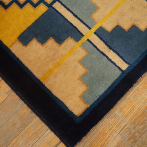 Close-up of a rug with bold geometric shapes in mustard yellow, tan, navy, and teal on wood planks.