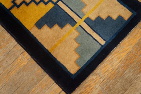 Close-up of a rug with bold geometric shapes in mustard yellow, tan, navy, and teal on wood planks.