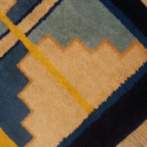 Navy, blue, teal, yellow, and tan geometric rug featuring stepped patterns on a distressed wood floor.