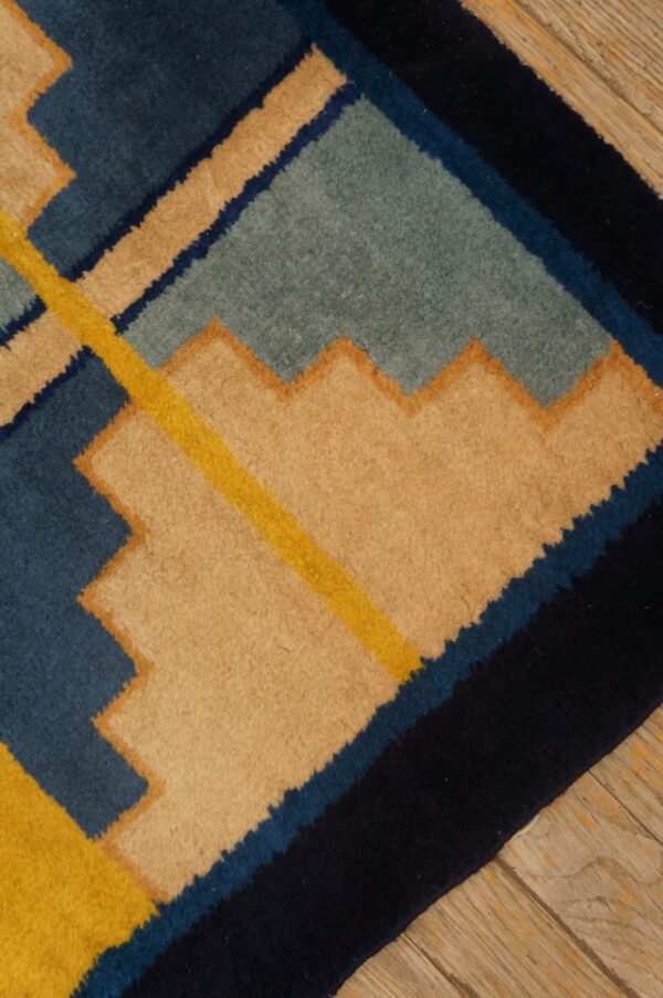 Navy, blue, teal, yellow, and tan geometric rug featuring stepped patterns on a distressed wood floor.