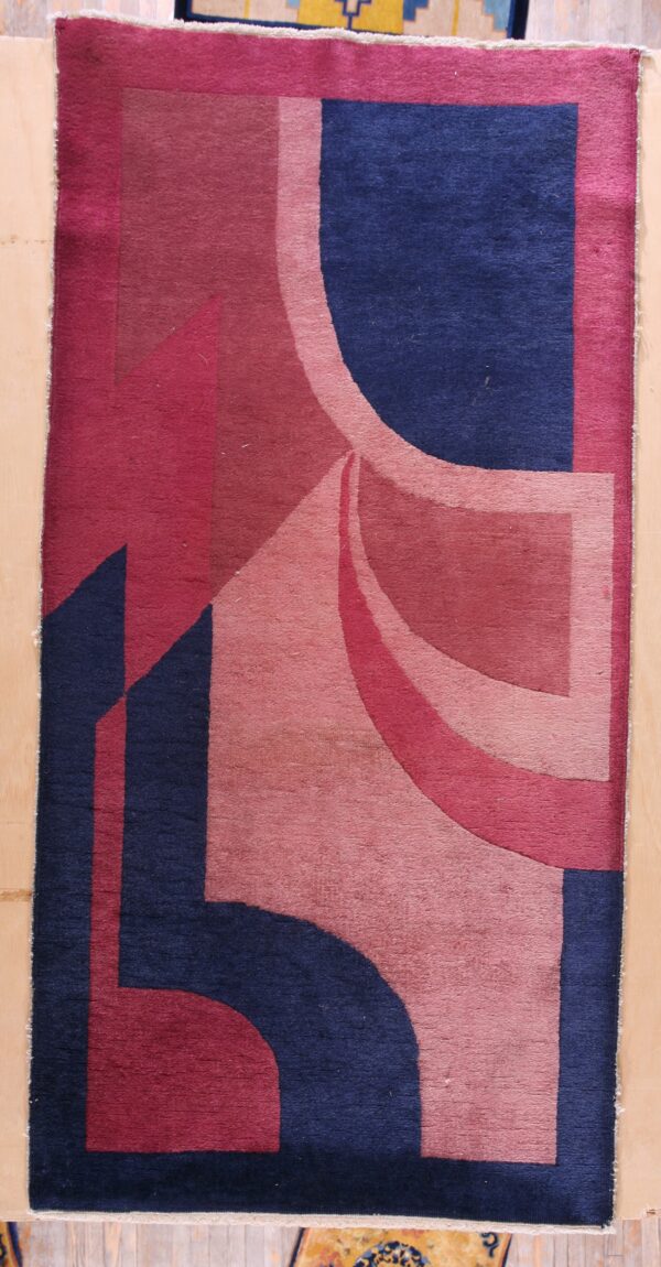 Abstract low-pile rug featuring bold geometric shapes in navy blue, magenta, and blush pink on a wood floor.