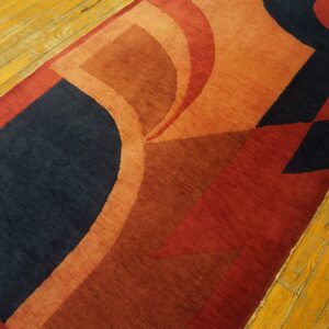 Curved and geometric shapes in navy, terracotta, and red on a short-pile rug over yellow wood planks.