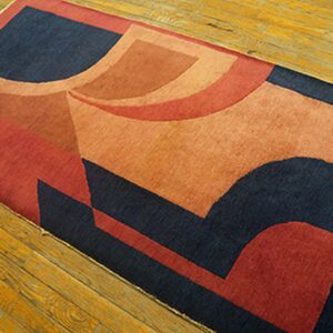 A runner rug with dark blue, rust, and orange abstract geometric shapes lies on wooden floorboards.
