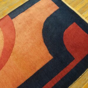 Navy, red, and orange geometric rug section resting on a worn, diagonally-laid yellow wood floor.