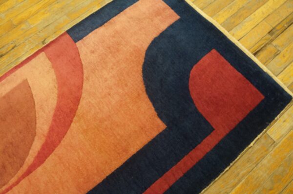 Navy, red, and orange geometric rug section resting on a worn, diagonally-laid yellow wood floor.