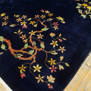 Dark blue rug with stylized yellow, pink, and green floral branches covers light distressed wood floors.