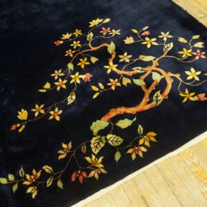 Navy rug with a stylized yellow, green, and red flowering branch on light wood floorboards.