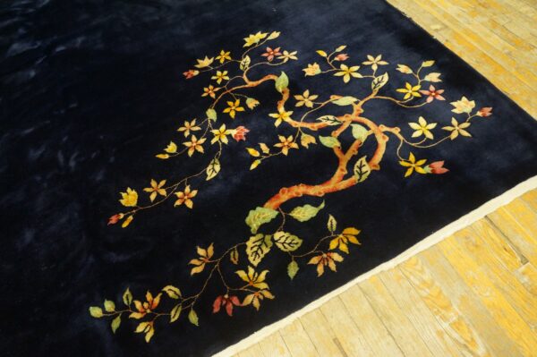Navy rug with a stylized yellow, green, and red flowering branch on light wood floorboards.