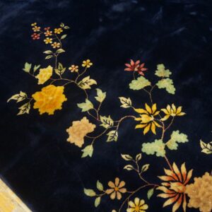 High-pile navy blue rug detailed with yellow and green vines and flowers rests on distressed wood flooring.