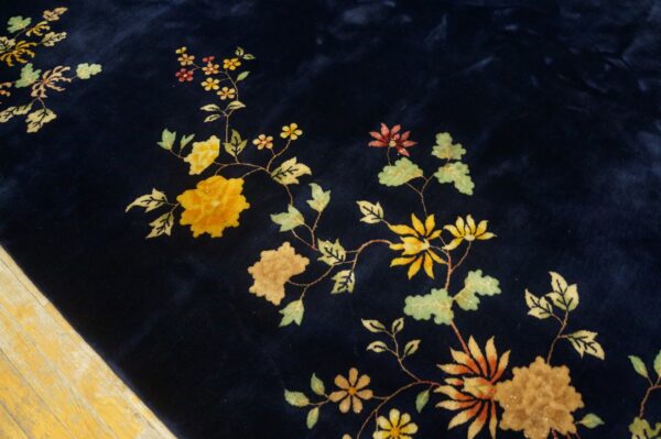 High-pile navy blue rug detailed with yellow and green vines and flowers rests on distressed wood flooring.