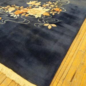 Deep blue high-pile rug with stylized cream and orange floral pattern on brightly lit wooden floorboards.