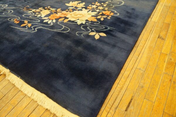 Deep blue high-pile rug with stylized cream and orange floral pattern on brightly lit wooden floorboards.
