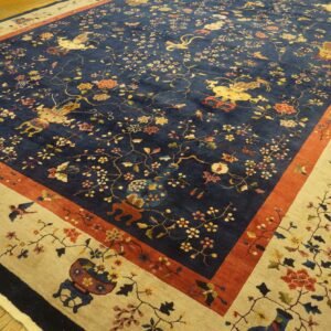 Ornate dark blue rug with multicolored florals, figures, and wide beige border, lying on hardwood floor.