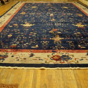 A large dark blue rug with intricate multi-color floral designs and light beige borders on polished wooden flooring.