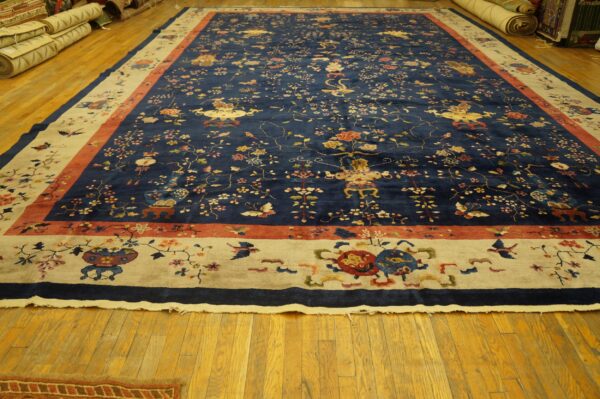 A large dark blue rug with intricate multi-color floral designs and light beige borders on polished wooden flooring.