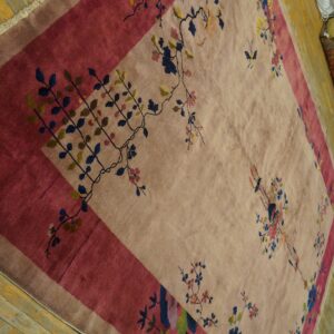 A pale tan rug with a magenta border features colorful floral and vine motifs on distressed wood floors.