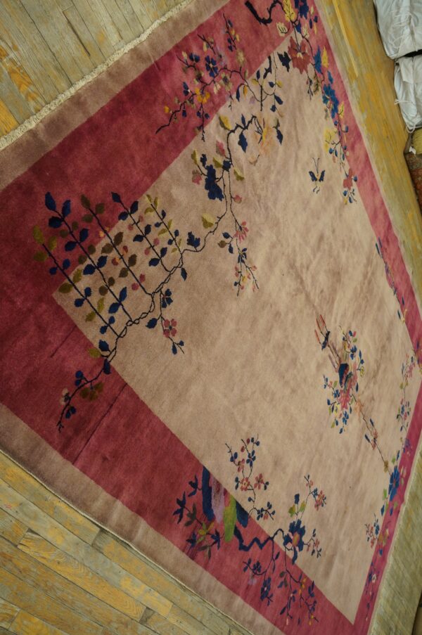 A pale tan rug with a magenta border features colorful floral and vine motifs on distressed wood floors.