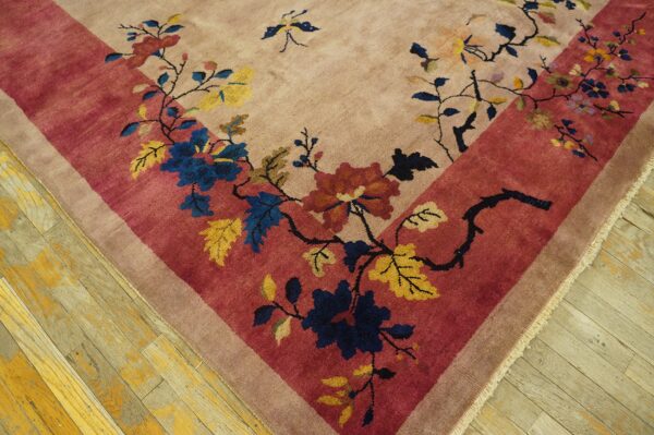 Floral rug corner in beige and pink with blue, rust, and yellow blooms, resting on distressed wood planks.