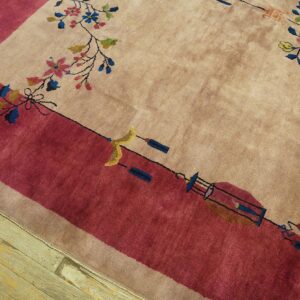 Beige rug with a deep rose border and multicolored floral pattern resting on distressed wood floors.