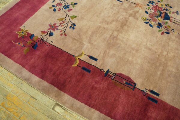 Beige rug with a deep rose border and multicolored floral pattern resting on distressed wood floors.