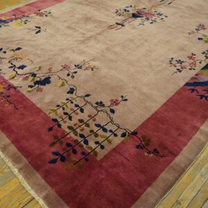 A beige rug with a wide magenta border patterned with colorful floral branches rests on rustic wood flooring.