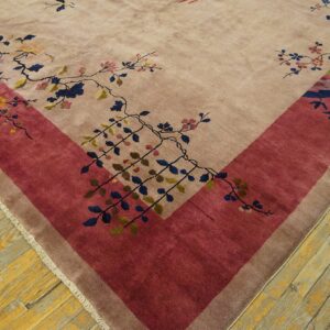 High-pile taupe rug corner with detailed floral vines and a wide crimson border on wood planks.