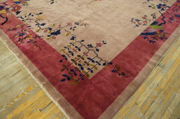 High-pile taupe rug corner with detailed floral vines and a wide crimson border on wood planks.
