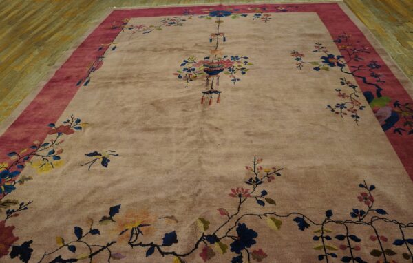 A plush rug with a pink-mauve field, magenta border, and scattered blue, yellow, and pink floral designs on wood flooring.