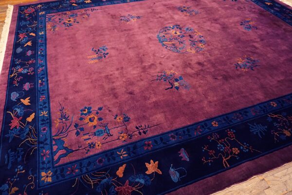 Purple rug with medium pile, scattered floral motifs, and a wide navy blue patterned border on wood floor.