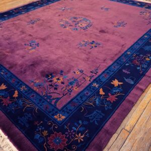 Velvety purple rug with multicolored scattered floral motifs and a wide dark blue patterned border on wood floor.
