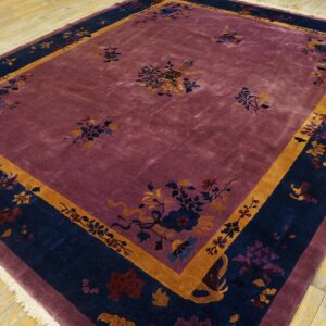 Deep purple rug with wide navy and gold floral borders on light yellow wooden flooring.