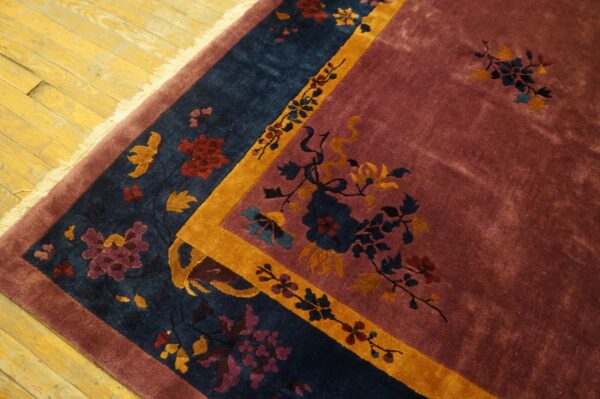 Mauve rug with detailed blue, yellow, and red floral borders sits on worn yellow wood flooring.