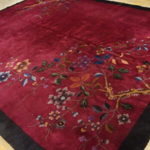 Dark red rug with black border featuring multicolored floral and vine motifs on distressed wood.