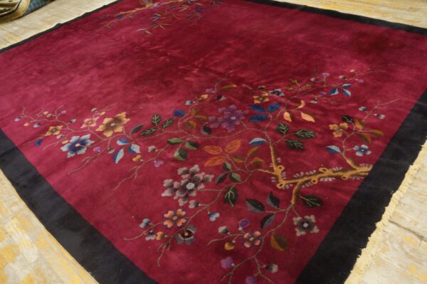 Dark red rug with black border featuring multicolored floral and vine motifs on distressed wood.