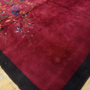 Deep red rug featuring an intricate floral vine design, black border, and fringe on wood planks.
