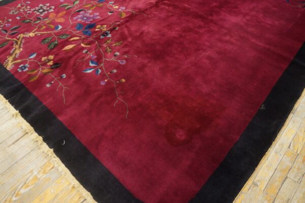 Deep red rug featuring an intricate floral vine design, black border, and fringe on wood planks.