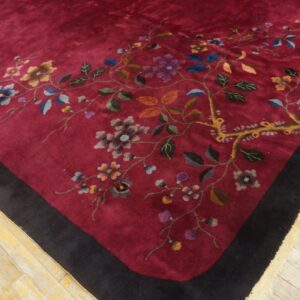 Deep maroon rug with a colorful floral vine pattern and black border rests on weathered wooden floors.