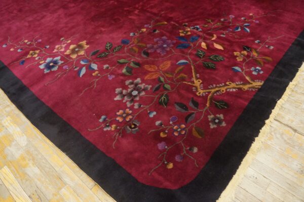 Deep maroon rug with a colorful floral vine pattern and black border rests on weathered wooden floors.