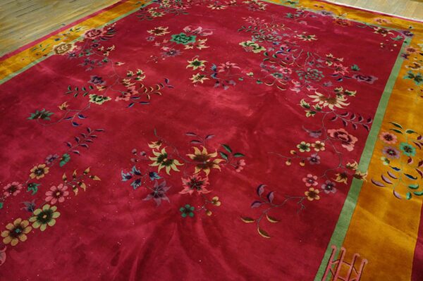 Deep magenta rug with high sheen, green and pink floral pattern, and a wide gold border on wood floor.