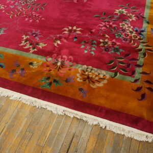 High-pile rug with a magenta field, multi-color florals, an orange border, and white fringe on hardwood flooring.
